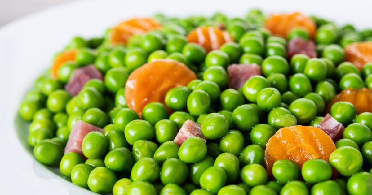 Green peas with serrano ham and carrot on wooden table